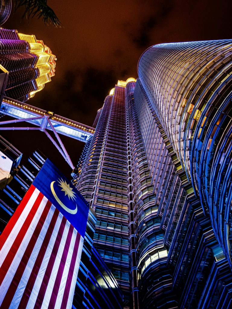 Dramatic view of Petronas Twin Towers illuminated at night with the Malaysian flag.