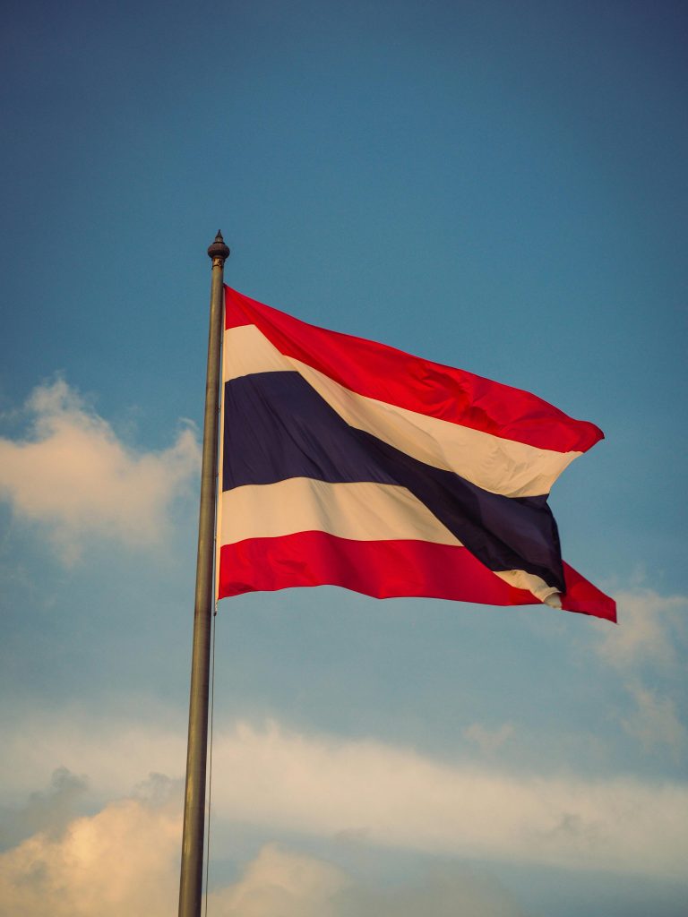 Thailand national flag on pole waving in the clear blue sky, symbolizing patriotism.